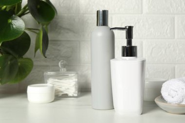 Farklı banyo aksesuarları ve kişisel bakım ürünleri tuğla duvarın yanındaki beyaz masada.