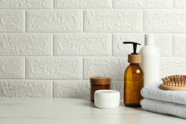 Farklı banyo aksesuarları ve kişisel bakım ürünleri tuğla duvarın yanındaki beyaz masada, metin için yer var.