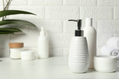 Farklı banyo aksesuarları ve kişisel bakım ürünleri tuğla duvarın yanındaki beyaz masada.