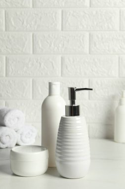 Banyo aksesuarları. Tuğla duvarın yanındaki beyaz masada kişisel bakım ürünleri
