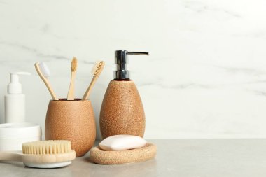 Beyaz mermer duvarın yanındaki gri masada farklı banyo aksesuarları ve kişisel bakım ürünleri var.