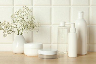 Banyo aksesuarları. Farklı kişisel bakım ürünleri ve vazodaki çingene çiçekleri beyaz kiremitli duvarın yanındaki ahşap masada.