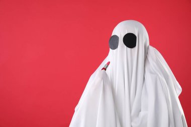 Modaya uygun bir hayalet. Kırmızı arkaplana ruj süren beyaz çarşaflı kadın, metin için boşluk