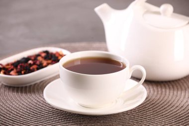 Fincanda romatik çay, çay tabağı, çaydanlık ve masada kuru çiçek yaprakları.