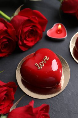 Sevgililer Günü. Lezzetli kalp şeklinde pasta, güller ve mum siyah masada, yakın plan.