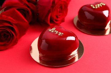 Sevgililer Günü. Lezzetli kalp şeklinde pastalar ve kırmızı arka planda güller, yakın plan.