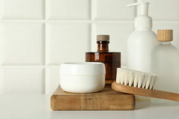 Bath accessories. Personal care products and wooden brush on white table near tiled wall, closeup