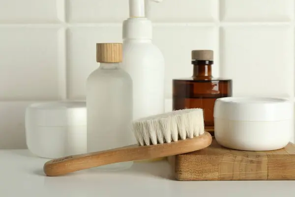 Bath accessories. Personal care products and wooden brush on white table near tiled wall, closeup