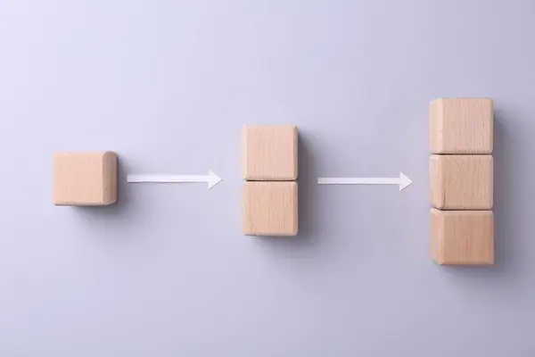 Business process organization and optimization. Scheme with wooden cubes and arrows on light grey background, top view
