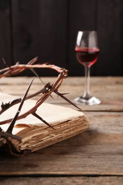 Crown of thorns, Bible and glass with wine on wooden table, selective focus