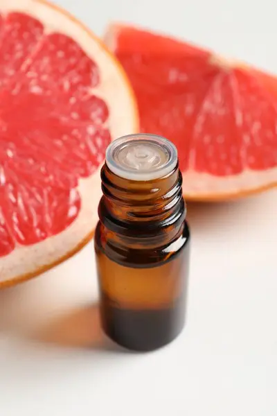 Grapefruit essential oil in bottle and fruit on white table
