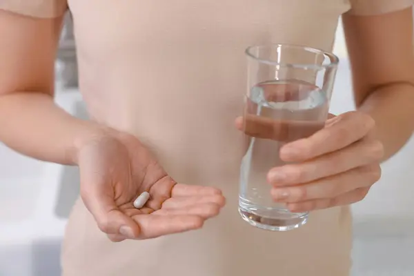 Beautiful young woman with vitamin pill and glass of water, closeup