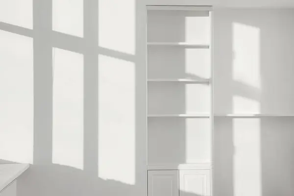 Light and shadows from window on wall and shelving unit indoors