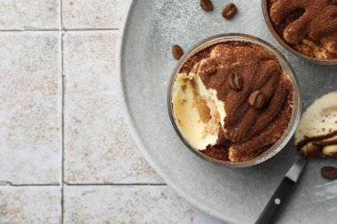 Bardaklar, kaşık ve kahve çekirdekleri içinde nefis tiramisu, açık fayanslı masa, üst manzara. Metin için boşluk