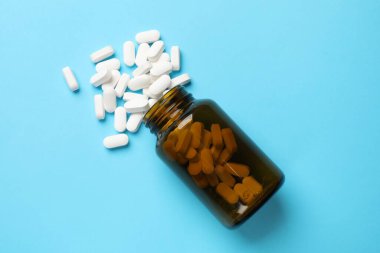 Açık mavi zemin üzerinde şişe ve vitamin kapsülleri, üst görünüm