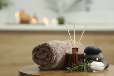 Spa kompozisyonu. Yuvarlak havlu, aroma yayıcı, masaj taşları ve yanan mumlar kapalı bir masada. Metin için boşluk