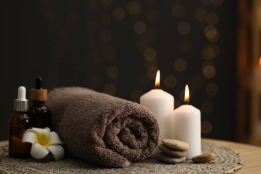 Spa kompozisyonu. Yuvarlak havlu, kozmetik ürünler, taşlar, yanan mumlar ve kapalı masa üzerindeki tesisat çiçeği, yakın plan. Metin için boşluk
