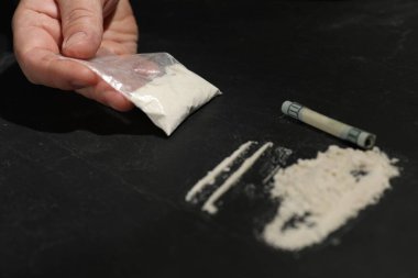 Uyuşturucu bağımlılığı. Koyu dokuma masasında kokain ve dolar banknotları olan bir adam, yakın plan.