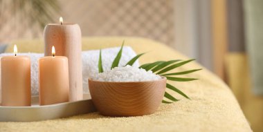 Spa kompozisyonu. Yumuşak sarı yüzeyde yanan mumlar, deniz tuzu ve havlu, metin için alan