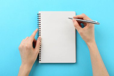 Açık mavi arkaplanda deftere yazan kadın, üst görünüm