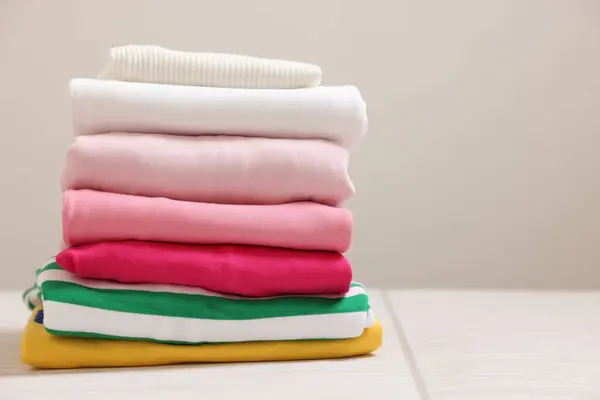 Stack of folded clothes on white table against grey background, space for text
