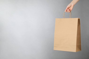 Gri arka planda Kraft kağıt çantası tutan bir kadın, mesaj için yeri olan yakın plan. Tasarım için model