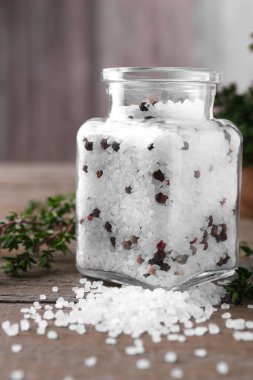 Cam kavanozda biberli tuz ve ahşap masada kekik.