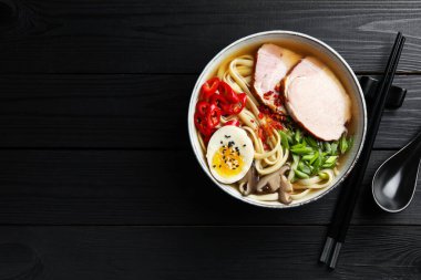 Lezzetli ramen kasede, kaşık ve çubuk çubuklar siyah ahşap masada, düzlük ve yazı için yer var. Erişte çorbası.