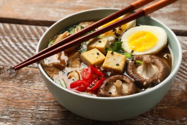 Bir kase lezzetli ramen ve yemek çubukları ahşap masada, yakın plan. Erişte çorbası.