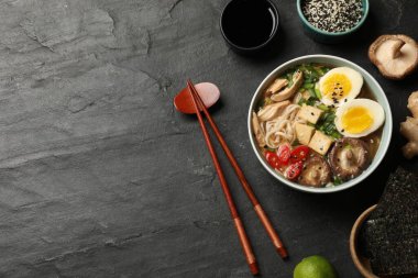 Erişte çorbası. Bir kase lezzetli ramen, malzemeler ve çubuklar siyah masada, düz konum. Metin için boşluk