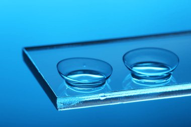 Mavi arkaplanda cam üzerine kontak lens, yakın plan.