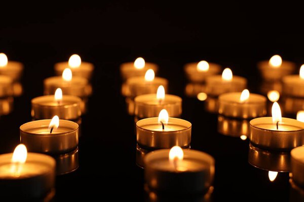 Burning candles on mirror surface in darkness, closeup