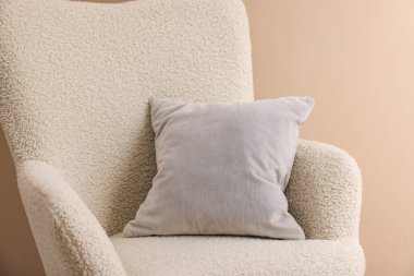 Bej duvarın yanındaki koltukta yumuşak gri yastık.