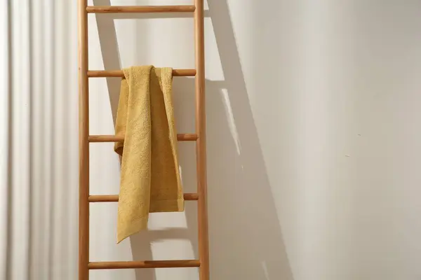 Yellow towel hanging on wooden ladder indoors. Space for text