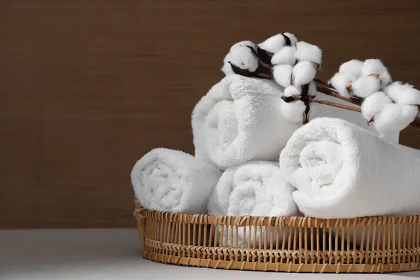 Rolled soft towels and cotton branch on white table indoors, space for text
