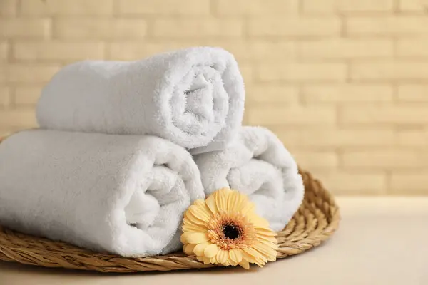 Rolled terry towels and flower on white table near brick wall indoors, closeup. Space for text