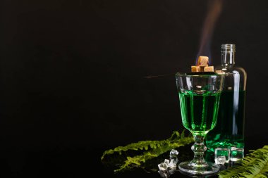 Absinthe, alevli kahverengi şeker, buz küpleri ve yeşil yapraklar ayna masasında, yazı için yer var. Alkolik içki.