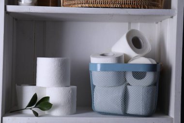 Tuvalet kağıdı ruloları ve beyaz rafta yeşil yapraklar.