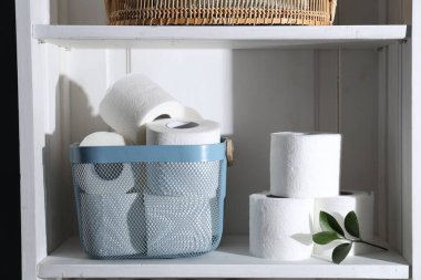 Tuvalet kağıdı ruloları ve beyaz rafta yeşil yapraklar.