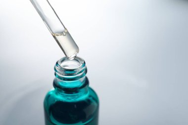 Açık gri arka planda pipetten şişeye nemlendirici serum damlatıyor. Yakın plan. Metin için boşluk