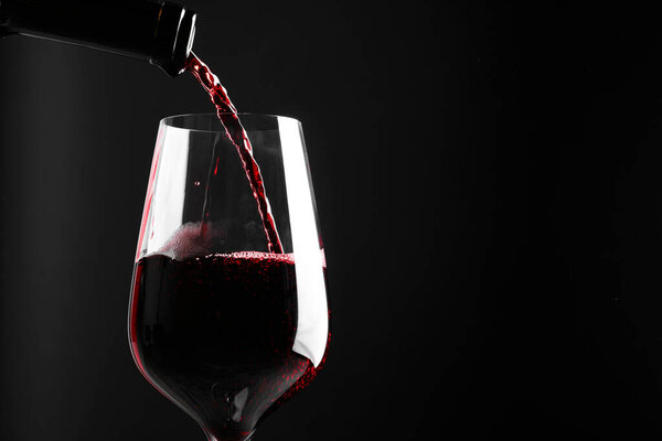 Pouring red wine into glass against black background, closeup. Space for text