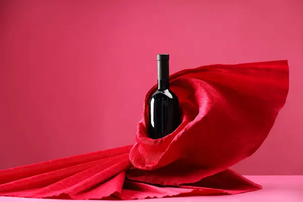 Stylish presentation of delicious red wine in bottle on pink background. Space for text