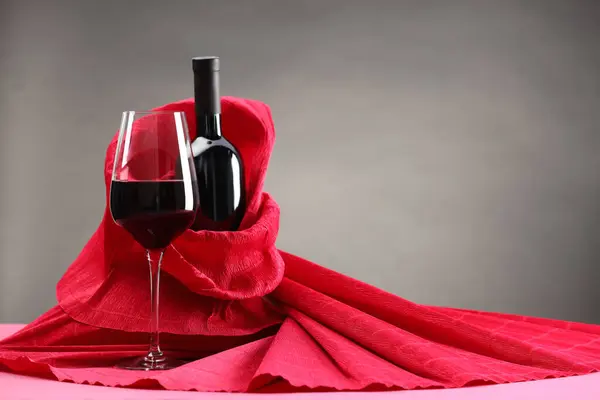 Stylish presentation of delicious red wine in bottle and glass on pink table against grey background. Space for text