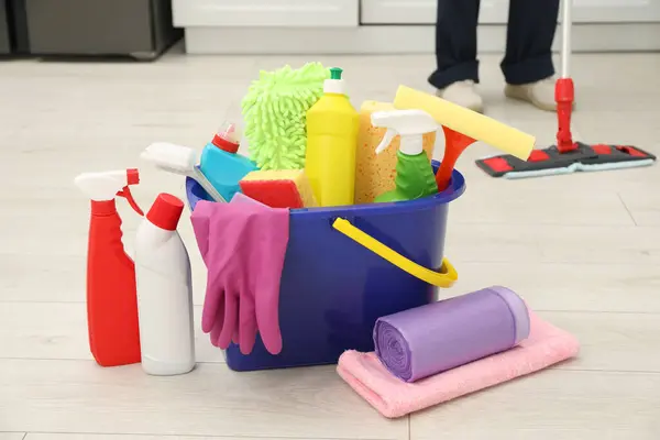 Different cleaning supplies in bucket and man mopping floor, selective focus
