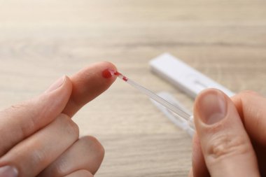 Laboratuvar testi. Masada pipetli parmaktan kan örneği alan kadın, yakın plan.