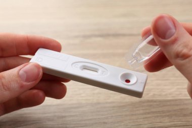 Tek kullanımlık test kasetinin üzerine tampon çözeltisi atan kadın masadaki, kapat