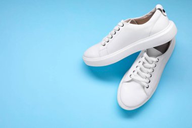 Açık mavi arka planda bir çift şık beyaz spor ayakkabı, üst manzara. Metin için boşluk