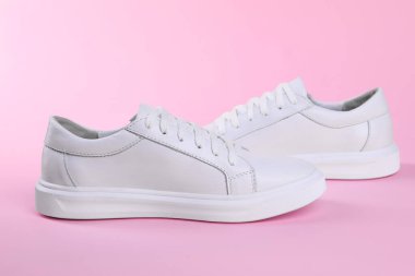 Pembe arka planda bir çift şık beyaz spor ayakkabı