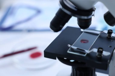 Laboratuvarda kırmızı sıvı numunesiyle modern tıbbi mikroskop, yakın plan. Metin için boşluk