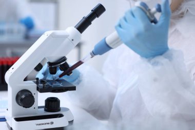 Laboratuvarda mikroskopla çalışırken cam kaydırağın üzerine kan damlatan bir bilim adamı.